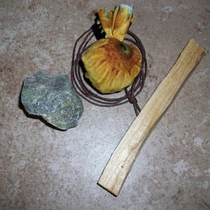May include: A small yellow fabric pouch tied with twine, a piece of wood, and a green rock on a brown surface.