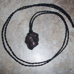 May include: A dark red gemstone pendant wrapped in black cord, hanging from a black cord necklace.