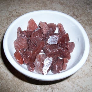 May include: A white bowl filled with a variety of small, irregularly shaped, reddish-brown crystals.