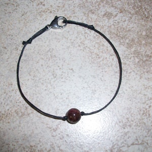 Puede incluir: Un brazalete simple de cordón negro con una sola cuenta de piedra roja oscura.