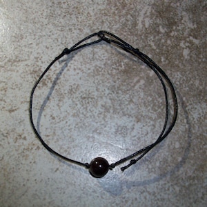Puede incluir: Un brazalete simple de cordón negro con una sola cuenta marrón oscura.