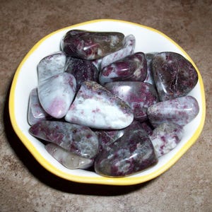 May include: A bowl of tumbled stones with a mix of white, gray, and purple colors. The stones are smooth and polished.
