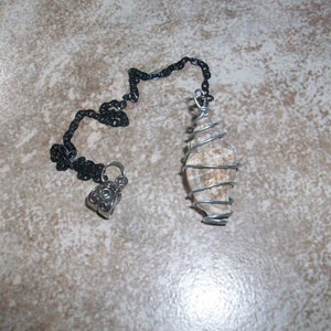 May include: A silver chain with a black chain attached to a silver pendant. The pendant is a rock wrapped in silver wire.