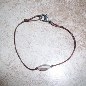 Puede incluir: Un brazalete de cordón marrón con una cuenta ovalada blanca y marrón.