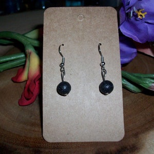 May include: A pair of black lava stone earrings with silver hooks. The earrings are displayed on a brown card.