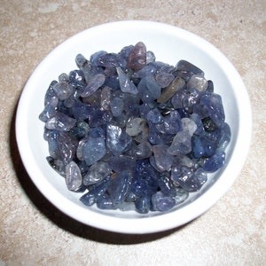 May include: A white bowl filled with a large quantity of small, light blue and purple gemstones.