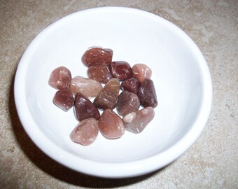 May include: A small white bowl filled with tumbled stones in shades of brown, pink, and red.