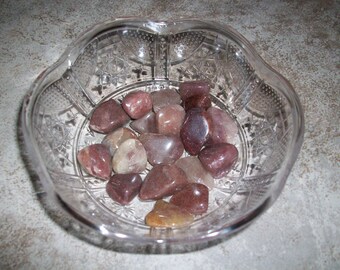 May include: A glass bowl filled with smooth, polished stones in shades of pink, brown, and white. The stones are arranged in a random pattern.