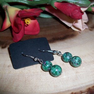 May include: A pair of silver dangle earrings with green and black speckled round beads.