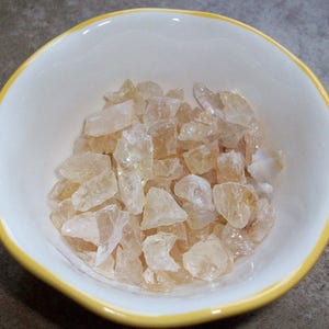 May include: A white bowl with a yellow rim filled with translucent, amber-colored, irregularly shaped crystals.