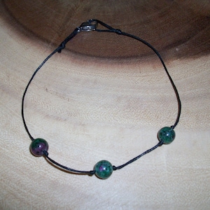 May include: A black cord necklace with three green and pink gemstone beads.