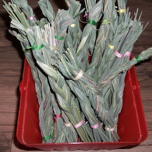 May include: A red plastic basket filled with bundles of dried, braided grass. The bundles are tied with colorful string in shades of pink, green, and yellow.