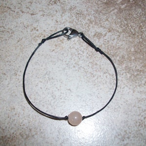 May include: A simple black cord bracelet with a single light pink bead.