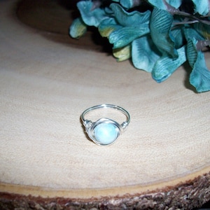 May include: A silver wire wrapped ring with a light blue gemstone.