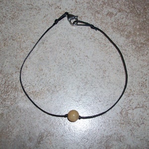 May include: A simple black cord necklace with a single light brown bead.