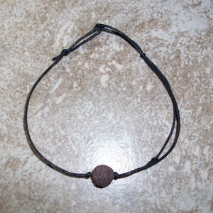 May include: A black cord necklace with a small, dark brown lava rock bead.