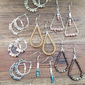 May include: Assortment of handmade beaded earrings in various styles and colors. The earrings feature different shapes, including hoops, teardrops, and triangles. The beads are made of natural stones, glass, and wood.