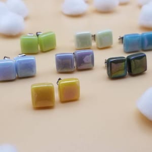 May include: Assortment of square-shaped earrings in various colors, including light blue, green, yellow, purple, and iridescent green. The earrings are made of glass and have a silver-toned post.