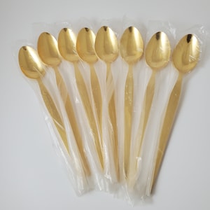 May include: A set of ten gold-colored teaspoons packaged in clear plastic. The spoons are arranged in a fan shape.