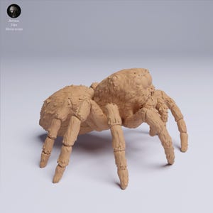 Puede incluir: Miniatura detallada de ara&ntilde;a de color marr&oacute;n claro con superficies texturizadas y m&uacute;ltiples patas. La ara&ntilde;a est&aacute; posada sobre un fondo neutro. El logotipo "Animal Den Miniatures" est&aacute; en la esquina superior izquierda.