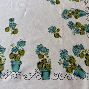 May include: White fabric with a repeating pattern of potted blue flowers with green leaves. The pots are teal, and the flowers are arranged in clusters. A black, swirled border frames the bottom edge of the fabric.