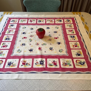 May include: A square tablecloth with a cream-colored center featuring small scattered illustrations of teapots and cups. A wide red border with a white grid pattern frames the center, containing larger square panels of kitchenware.