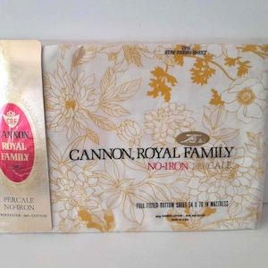 May include: A packaged Cannon Royal Family percale sheet set. The white sheet features a floral pattern in shades of gold. The packaging includes the text "The Stay Fresh Sheet" and "No-Iron Percale". The fitted sheet measures 54 x 76 inches.