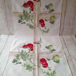 May include: White linen table runner with a repeating pattern of red tomatoes, green leaves, and light green gourds. The design is set against a light brown trellis. The edges of the runner are fringed.