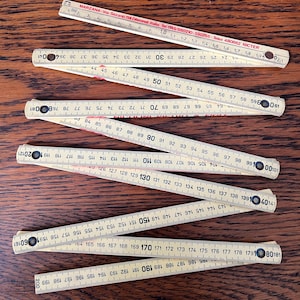 May include: A set of six wooden folding rulers with black and red markings. The rulers are numbered in inches and centimetres. The rulers are made by Marzana, an Italian company.
