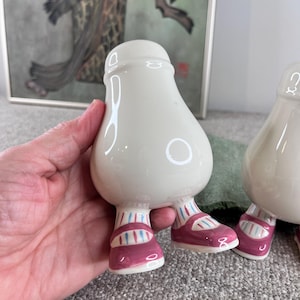 May include: Two white ceramic salt and pepper shakers shaped like people with pink and blue striped shoes.