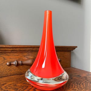 Peut inclure: Un vase en forme de goutte d'eau, d'un orange vif. Le vase présente une base claire et arrondie et un col fin et allongé. Ce vase décoratif en verre est une pièce d'accent frappante pour toute maison.