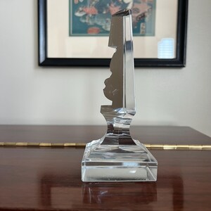 May include: A clear glass decorative object with a faceted design. The object has a square base and a tall, slender top.
