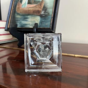May include: A clear glass pyramid-shaped bottle stopper with a square base.