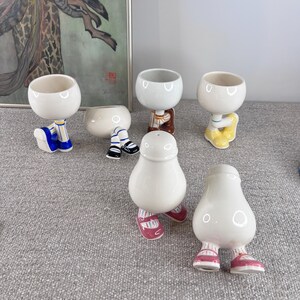 May include: Set of six white ceramic salt and pepper shakers with legs and painted details. The shakers are shaped like people and have different colored shoes and clothing.