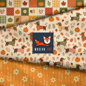 May include: Fabric featuring a patchwork pattern of pumpkins and leaves, a cream-colored section with dachshunds in sweaters and hats, and an orange section with white flowers. A square logo with a fox and the text MODERN FOX is centered.