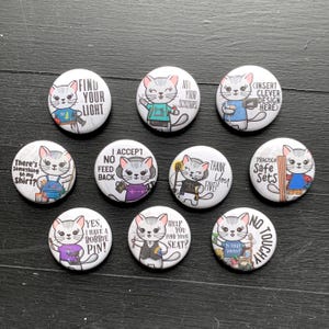 May include: Set of 10 round white button pins featuring a cartoon cat with different sayings. The sayings include "Find your light", "I accept no feed back", "There's something on my shirt", "No! Your scissors", "Insert clever design here", "Thank you five", "Practice safe sets", "Yes, I have a bobbie pin", "Help you find your seat", and "No touchy".