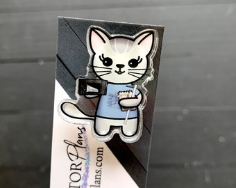 May include: A clear acrylic bookmark featuring a cartoon cat wearing a blue shirt and holding a cup of coffee and a book. The bookmark has the text "ACTOR Plans" and "actorplans.com" printed on it.