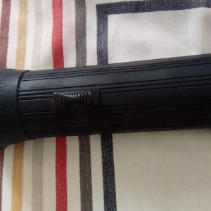 May include: A black flashlight with a ridged handle and a textured head. The word "READY" is embossed on the side. The flashlight has a switch and a ribbed design for grip.