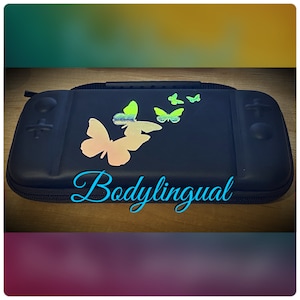 May include: A black carrying case with a zipper closure and a handle. The case is decorated with iridescent butterfly decals. The word "Bodylingual" is written in a cursive font across the bottom of the case.