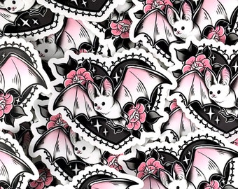 May include: A set of stickers featuring cute pink and white bats with black outlines. The bats are surrounded by black hearts with white lace trim and pink flowers. The stickers are perfect for adding a touch of whimsy to laptops, water bottles, or journals.