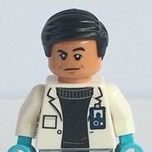 Op de afbeelding: Een Lego-minifiguur van een persoon met een witte labjas over een zwarte trui, grijze broek en blauwe handschoenen. De minifiguur heeft zwart haar en een serieuze uitdrukking. Een badge is zichtbaar op de labjas.