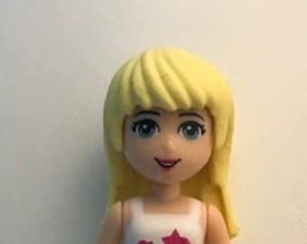 Puede incluir: Una muñeca rubia con una camisa rosa y blanca y pantalones cortos verdes. La muñeca tiene un diseño rosa y blanco en su camisa y un diseño rosa y blanco en sus pantalones cortos.