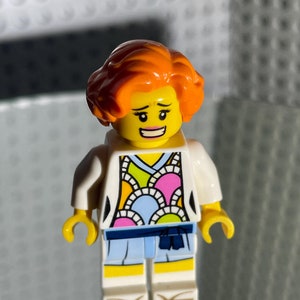 May include: A Lego minifigure of a woman with orange hair, wearing a white jacket over a colorful patterned shirt and blue pants. She has a yellow face with a smile and black eyebrows.