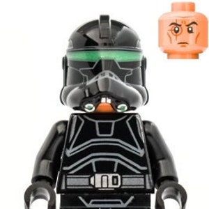 May include: A black and green Lego minifigure of a Star Wars clone trooper with a black helmet and a green visor. The minifigure has a black torso and legs with silver details. The minifigure is holding a black blaster rifle.