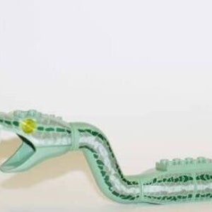 Puede incluir: Un juguete de serpiente de plástico verde con un diseño estampado y un ojo amarillo. La serpiente está enroscada en forma de espiral.