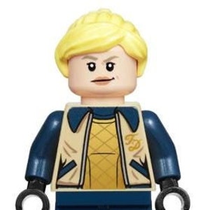 May include: A Lego minifigure of a woman with blonde hair, wearing a blue jacket with a yellow shirt underneath, and blue pants. The jacket has the letters "FD" on the front.