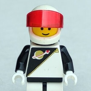 May include: A white Lego minifigure astronaut wearing a black and white spacesuit with a red visor and a gold zipper detail. The astronaut has a yellow face with a smile and black eyes.