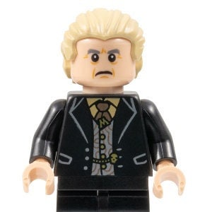 May include: A Lego minifigure of a man with blond hair, wearing a black suit, white shirt, and a gold tie. The minifigure has a serious expression on his face.