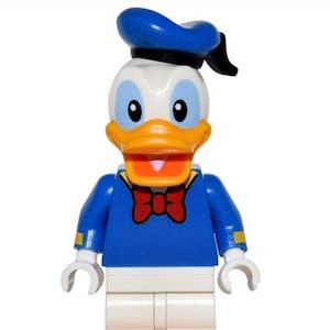 Puede incluir: Una figura de Lego de Pato Donald, con gorro de marinero azul, chaqueta azul, pantalones blancos y pies naranjas. La figura tiene un pico amarillo, una pajarita roja y manos blancas. Se encuentra sobre una base negra.
