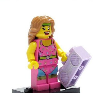 Pode incluir: Uma minifigura Lego de uma mulher vestindo um traje de treino rosa e azul com uma faixa de cabeça e segurando um toca-fitas roxo.